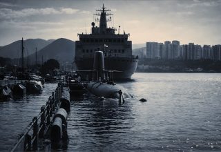 Naval ship and submarine docked in a harbor, representing maritime defence and engineering roles.