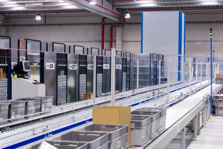 Automated warehouse conveyor carrying grey crates between storage racks