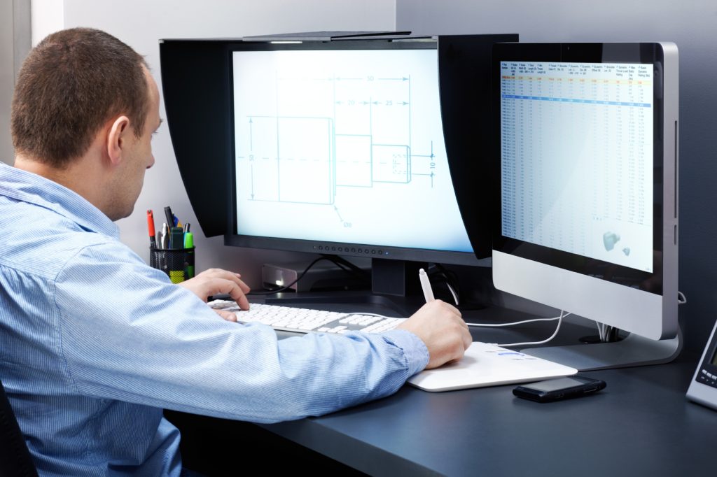 Engineer at a desk working on technical drawings across two computer monitors