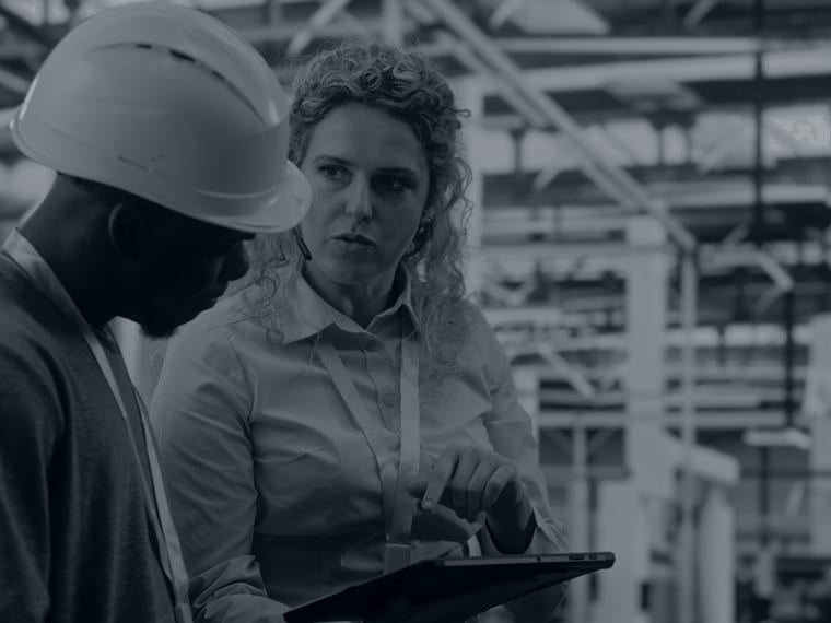 Engineering manager with a tablet briefing an engineer in a hard hat on the factory floor