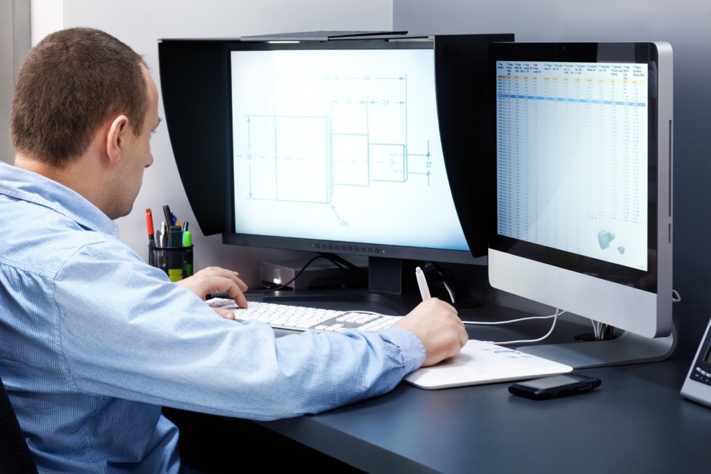 Engineer at a desk working on technical drawings across two computer monitors