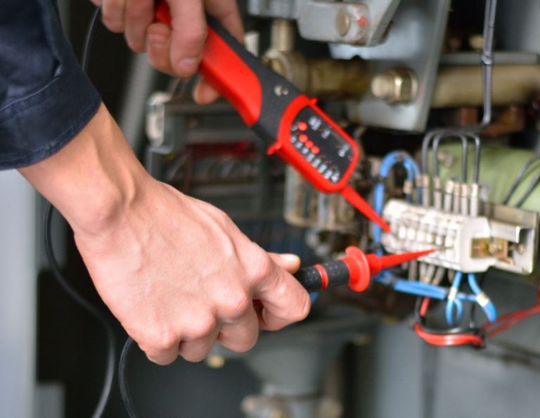 Electrician testing a terminal block in a control panel with a voltage tester