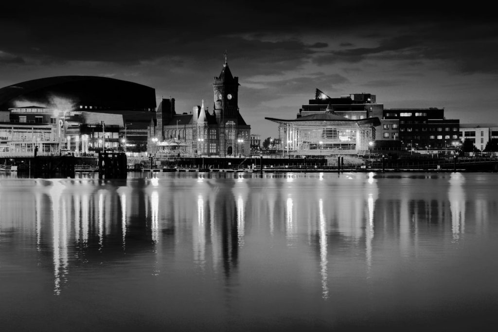 Cardiff Bay waterfront at night, with the Pierhead Building clock tower and nearby buildings reflected in still water