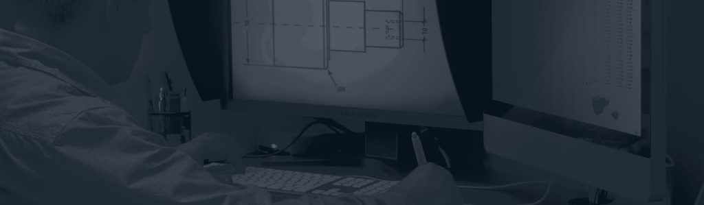 Engineer at a desk looking at a technical drawing of a machined part on a computer monitor, with a keyboard in front