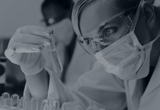 Laboratory scientist in goggles, mask and gloves examining a test tube